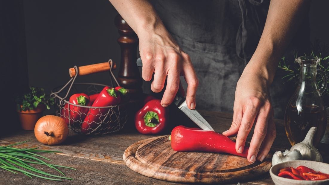 Chef chopping red pepper on a wooden chopping board